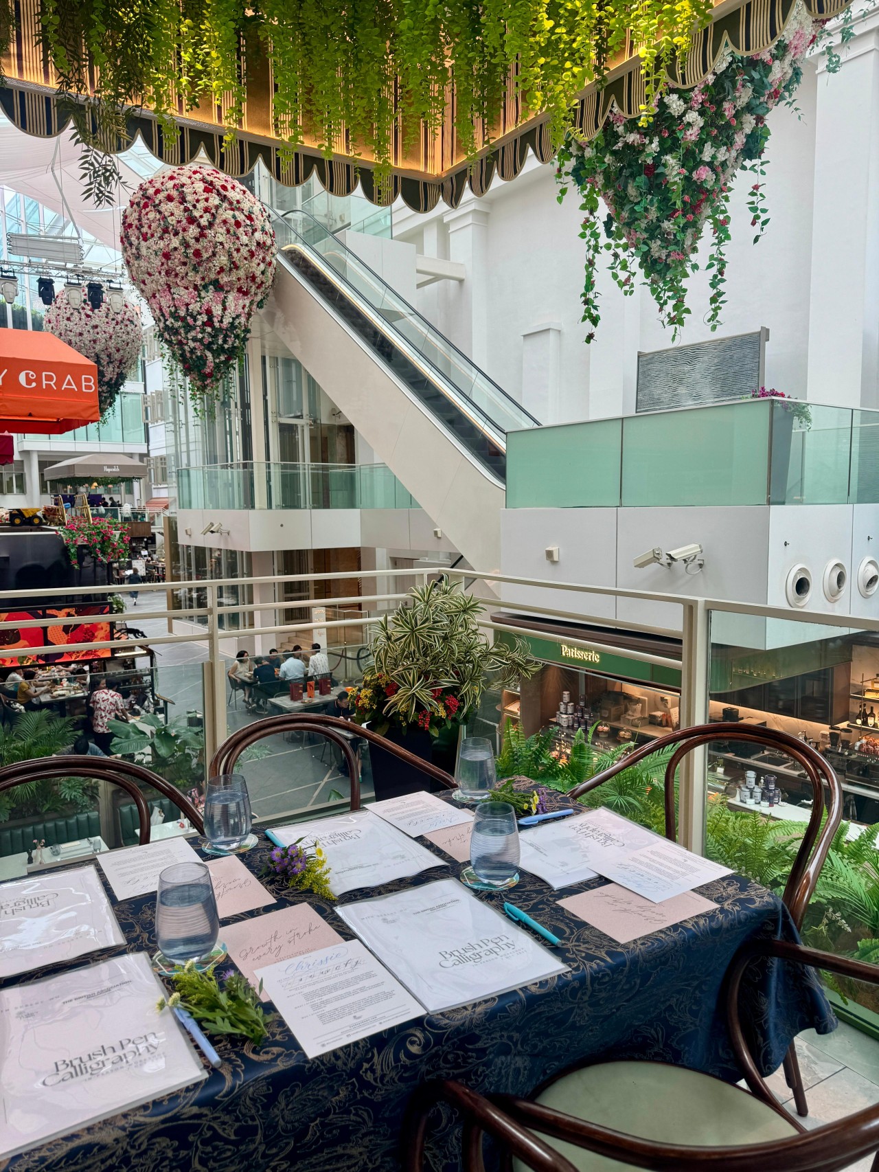Serene Wu hosting a calligraphy workshop with The British Association Singapore participants practicing brush lettering in a serene café setting.